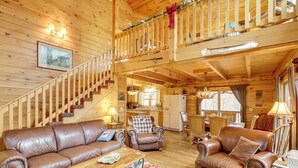 L’intérieur d’un chalet en bois comprend un escalier, des canapés en cuir, une table à manger et un coin cuisine.