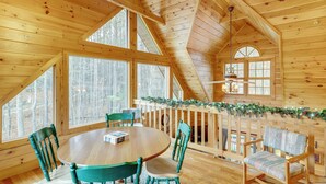 L’intérieur d’un chalet en bois, avec une table ronde et des chaises, de grandes fenêtres et une balustrade en bois agrémentée de verdure.