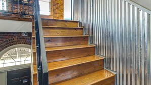 Eine Holztreppe mit Metallgeländern, einer Ziegelwand und einem Fenster mit Metallgitter.