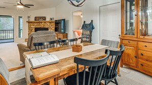 A dining area with a wooden table, black chairs, a chandelier, and a stone fireplace.
