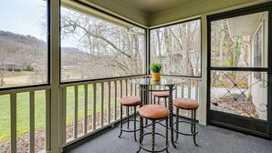 A covered outdoor seating area with a glass table and four stools, overlooking a landscaped garden and distant hills. - Franklin Golf Condo: '13th Hole Retreat'! (Franklin)