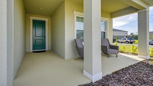 A covered porch with a teal door, two gray chairs, and a view of a street with parked cars. - Florida Snowbird Haven w/ Pool! Easy I-75 Access (Parrish)