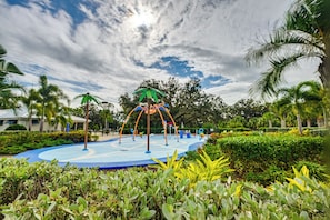 A playground with climbing structures and a blue play area surrounded by greenery and palm trees. - Florida Snowbird Haven w/ Pool! Easy I-75 Access (Parrish)