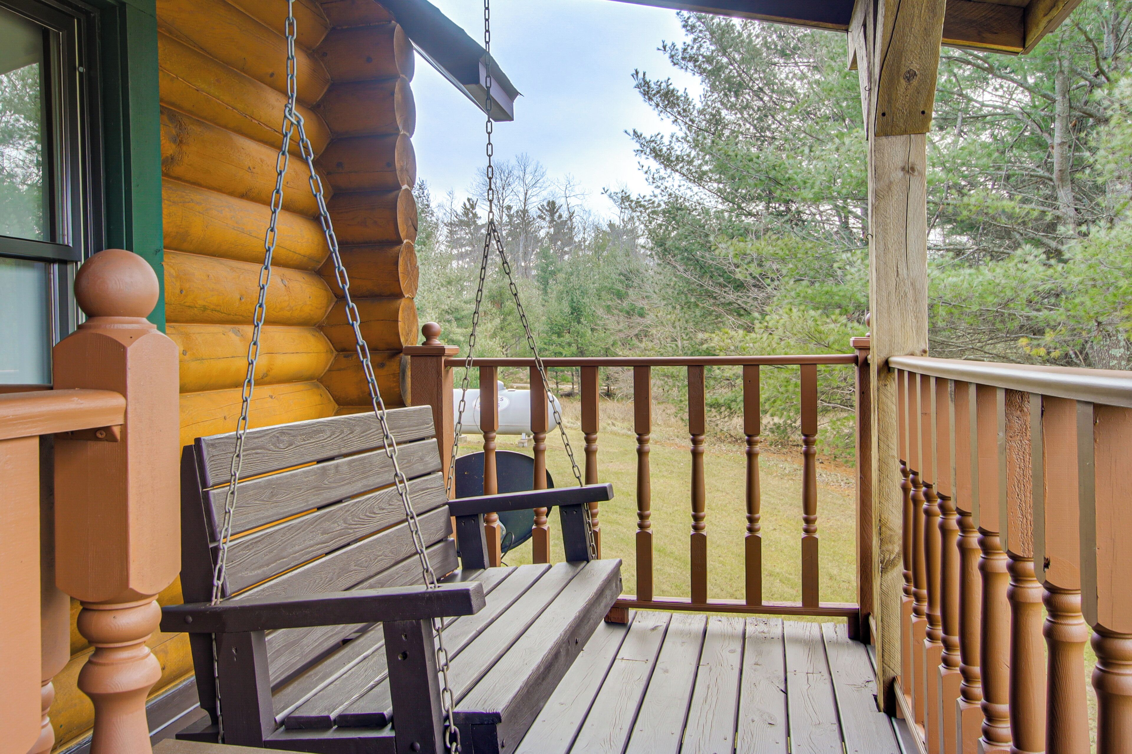 A wooden porch with a swing and a view of a forested area.