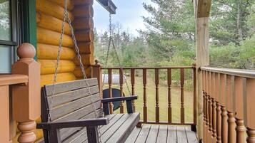 A wooden porch with a swing and a view of a forested area.
