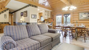A cozy cabin interior with a plaid sofa, wooden dining table, and a staircase leading to an upper level.