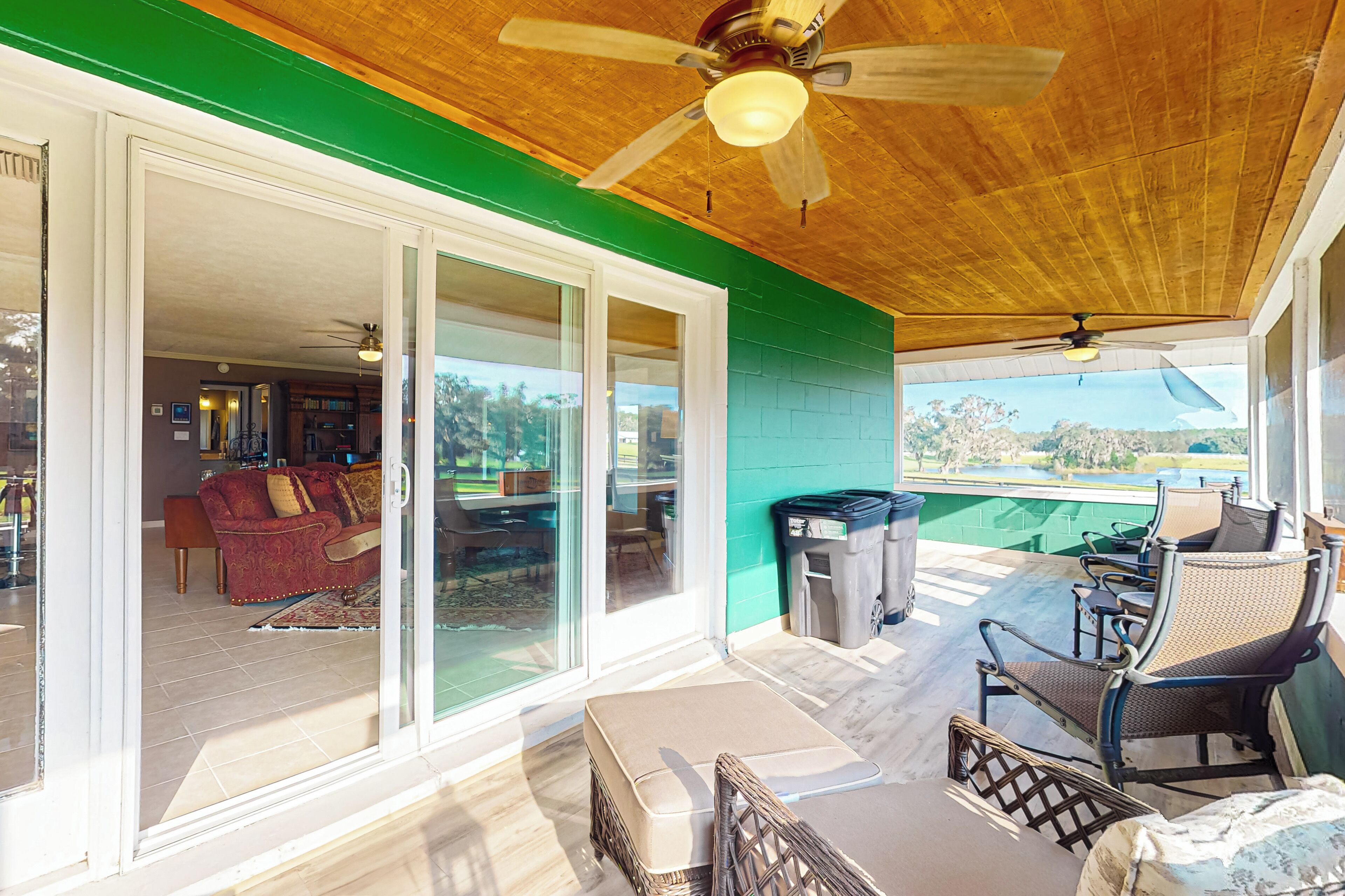 A covered patio with a ceiling fan, sliding glass doors leading to an indoor living area, outdoor furniture, and a view of a golf course.