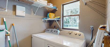 A laundry room with a front-loading washer and dryer, shelves with folded towels, a window, and a mop.