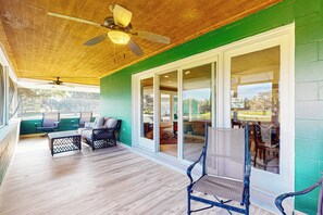 Une terrasse couverte avec un plancher en bois, un ventilateur de plafond et un espace salon comprenant des chaises et une table.