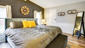 Ein Schlafzimmer mit einem großen Bett, einem Nachttisch, einem Spiegel und einem Fenster mit Vorhängen.