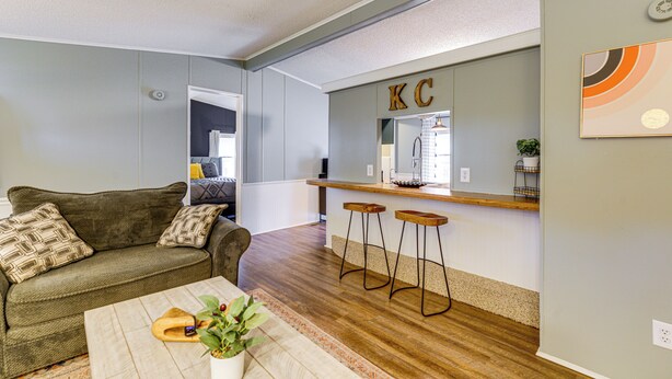 Ein Wohnzimmer mit Sofa, Couchtisch und einer Küchenzeile mit Bar und Barhocker.