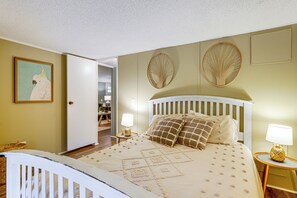 A bedroom with a white bed, beige walls, and a door leading to another room. - Port Austin Home Near Lake Huron w/ Fire Pit! (Port Austin)