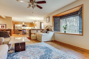A spacious living room with a large window, a ceiling fan, and a view of the kitchen.