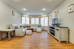 A living room with a sectional sofa, ottomans, a wooden coffee table, a TV stand, and a cabinet.