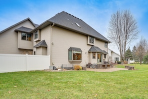 A two-story house with a covered patio, a fenced yard, and a large tree.