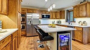 A modern kitchen with wooden cabinets, stainless steel appliances, a central island with stools, and a built-in refrigerator. - Rare Gem on a Ravine, Family Home in North Mankato (Mankato)