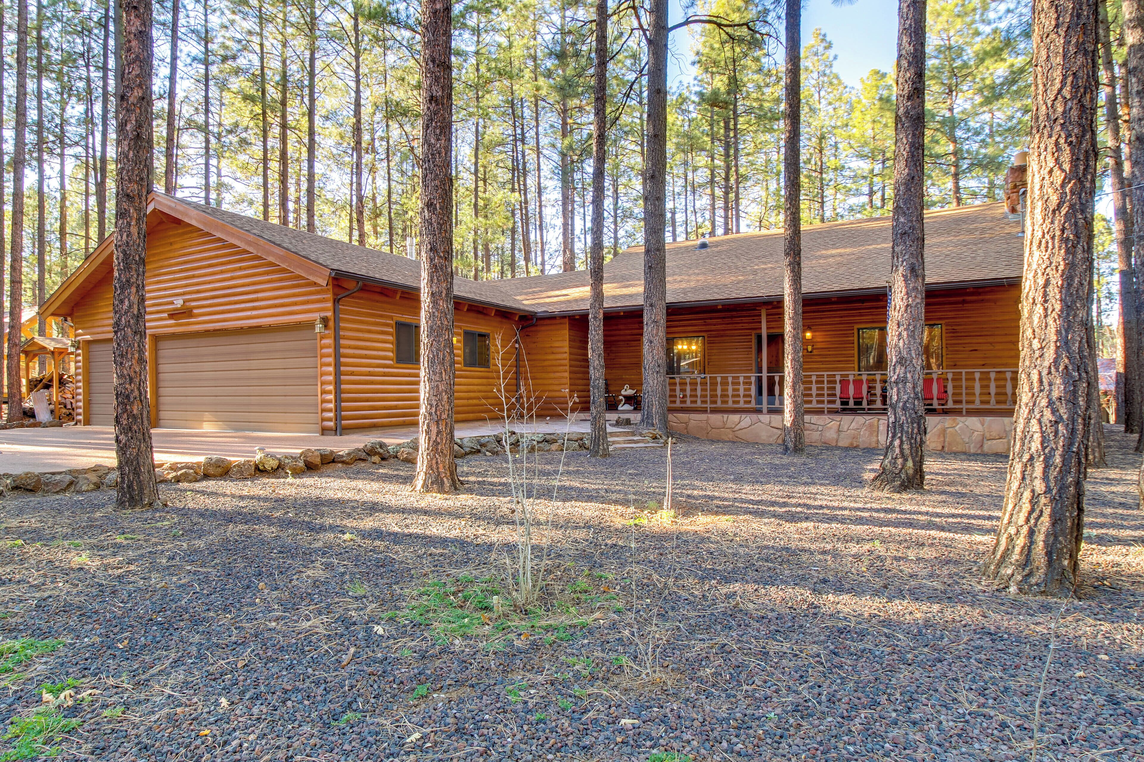 A log cabin with a large garage, surrounded by tall pine trees.