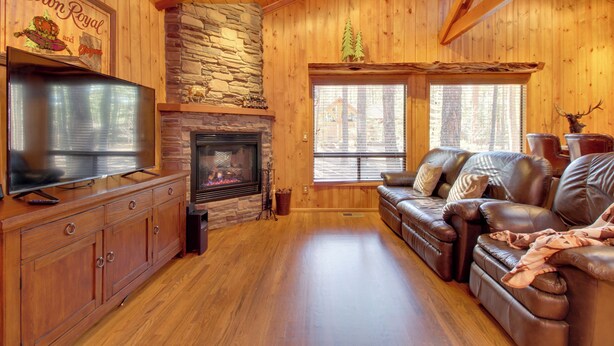 A cozy cabin interior with a stone fireplace, leather sofa, wooden walls, and a television on a wooden cabinet. - Bear's Den 2 Mi to Pinetop CC: Ski, Sled, Hike! (Pinetop)
