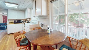 Een keuken met witte kasten, een houten eettafel en stoelen. Er is een raam met uitzicht.