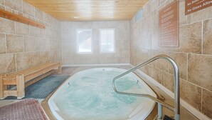 Una stanza spa con soffitto in legno, vasca idromassaggio e due finestre.