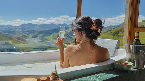 A person in a bathtub with a view of mountains, a bottle, and a bowl of strawberries. - Viso Villas Pousada Boutique (Sapucaí-Mirim)
