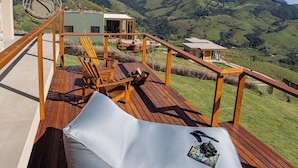 A wooden deck with a cushioned seating area, a hanging chair, and a view of a mountainous landscape. - Viso Villas Pousada Boutique (Sapucaí-Mirim)