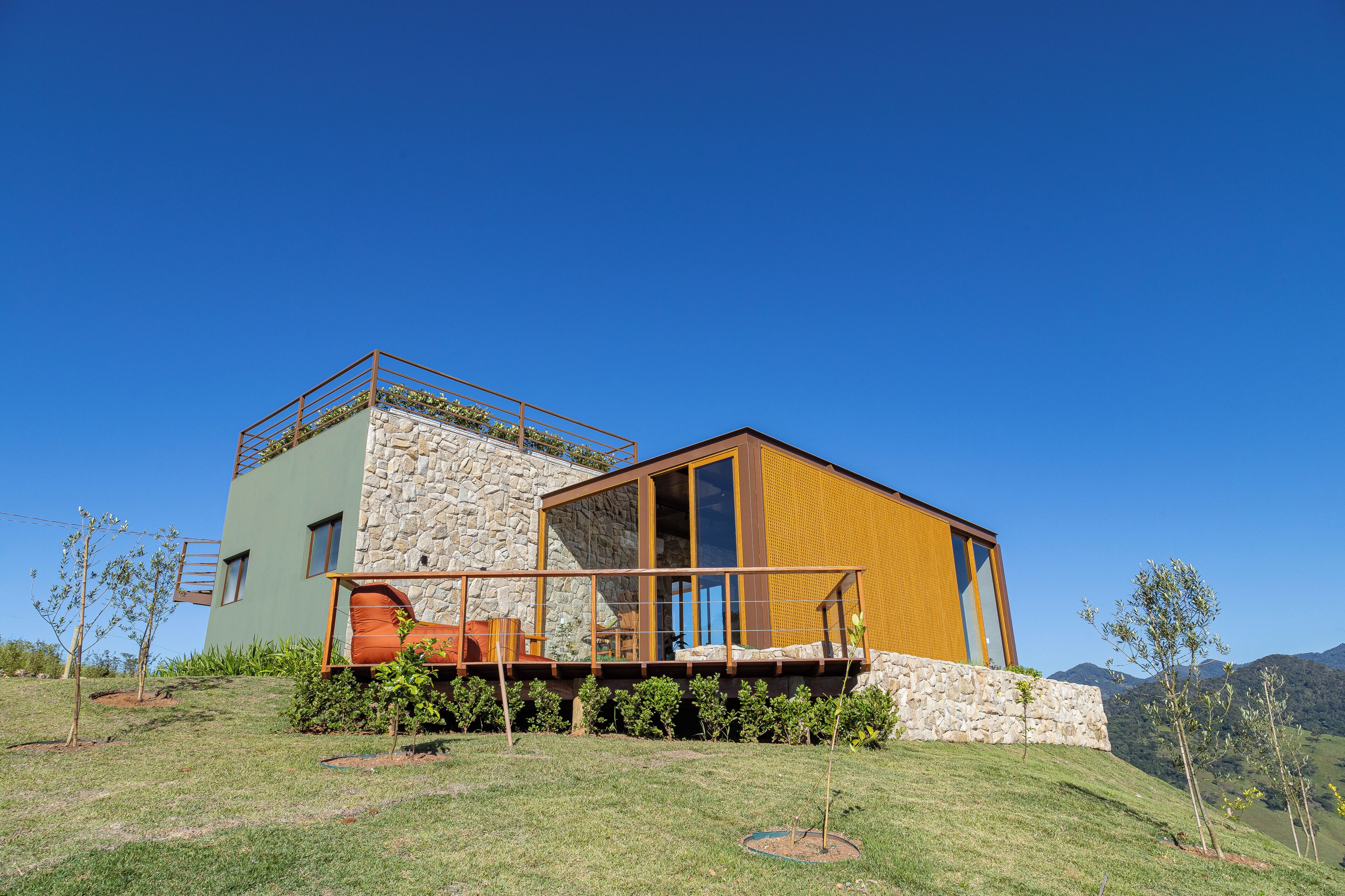 A modern two-story house with a stone facade, large windows, and a wooden deck.