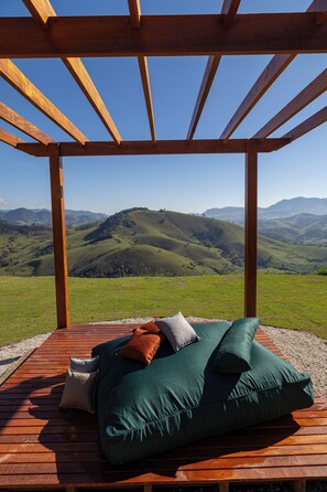 Une terrasse en bois avec un canapé vert et des coussins, offrant une vue sur un paysage montagneux.