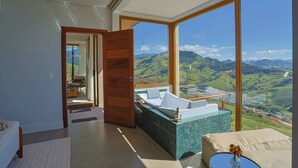 A modern hotel room with a large window offering a mountain view, a wooden door leading to a balcony, and a marble counter. - Viso Villas Pousada Boutique (Sapucaí-Mirim)
