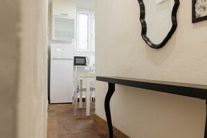 A narrow hallway leading to a kitchen area with white cabinetry, a microwave, and a dining table with chairs. - Pepi Comfort Apartment (Firenze)