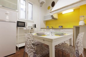 A kitchen with white appliances, a yellow wall, and a table with chairs. - Pepi Comfort Apartment (Firenze)