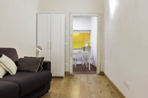 A room with a dark-colored sofa, a white door, and a yellow wall visible through an open door leading to a kitchen area with a table and chairs. - Pepi Comfort Apartment (Firenze)