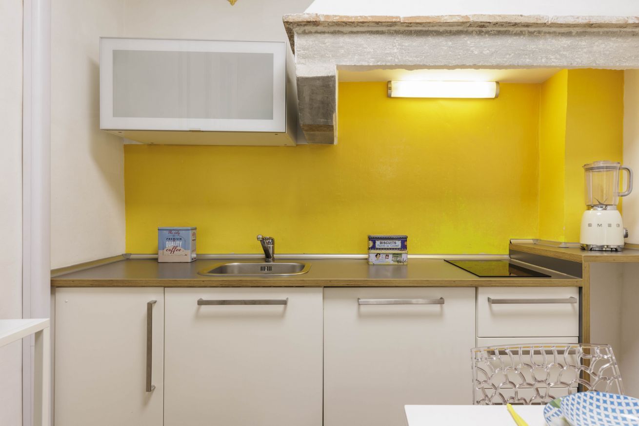 A kitchen with a yellow wall, white cabinets, a microwave, a sink, and a blender.