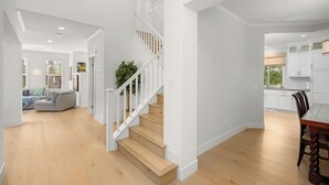 Ein geräumiger Wohnbereich mit einer Holztreppe, einem Esstisch und einer Küche im Hintergrund.