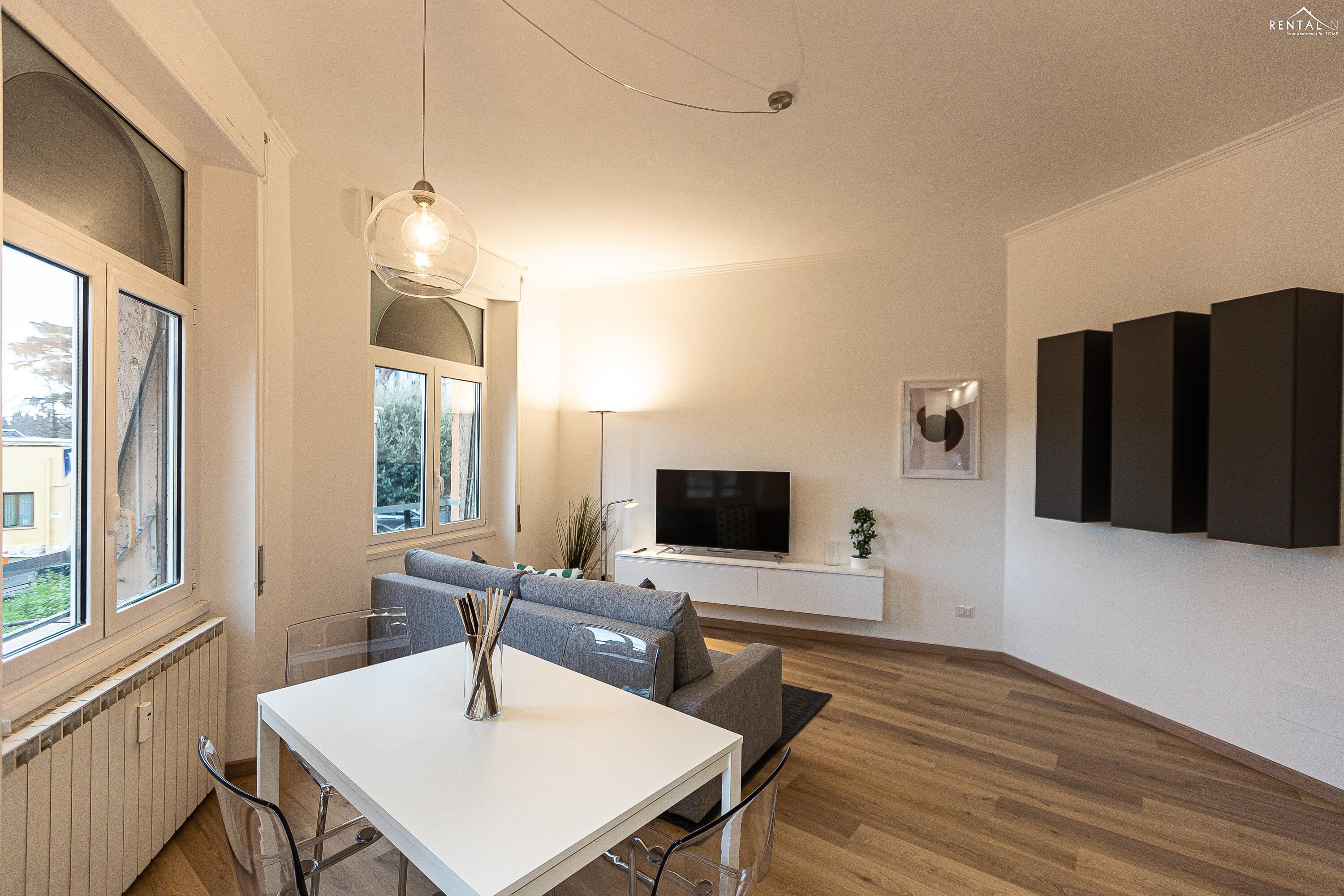 A modern living room with a white table, grey sofa, and a TV on a white stand.