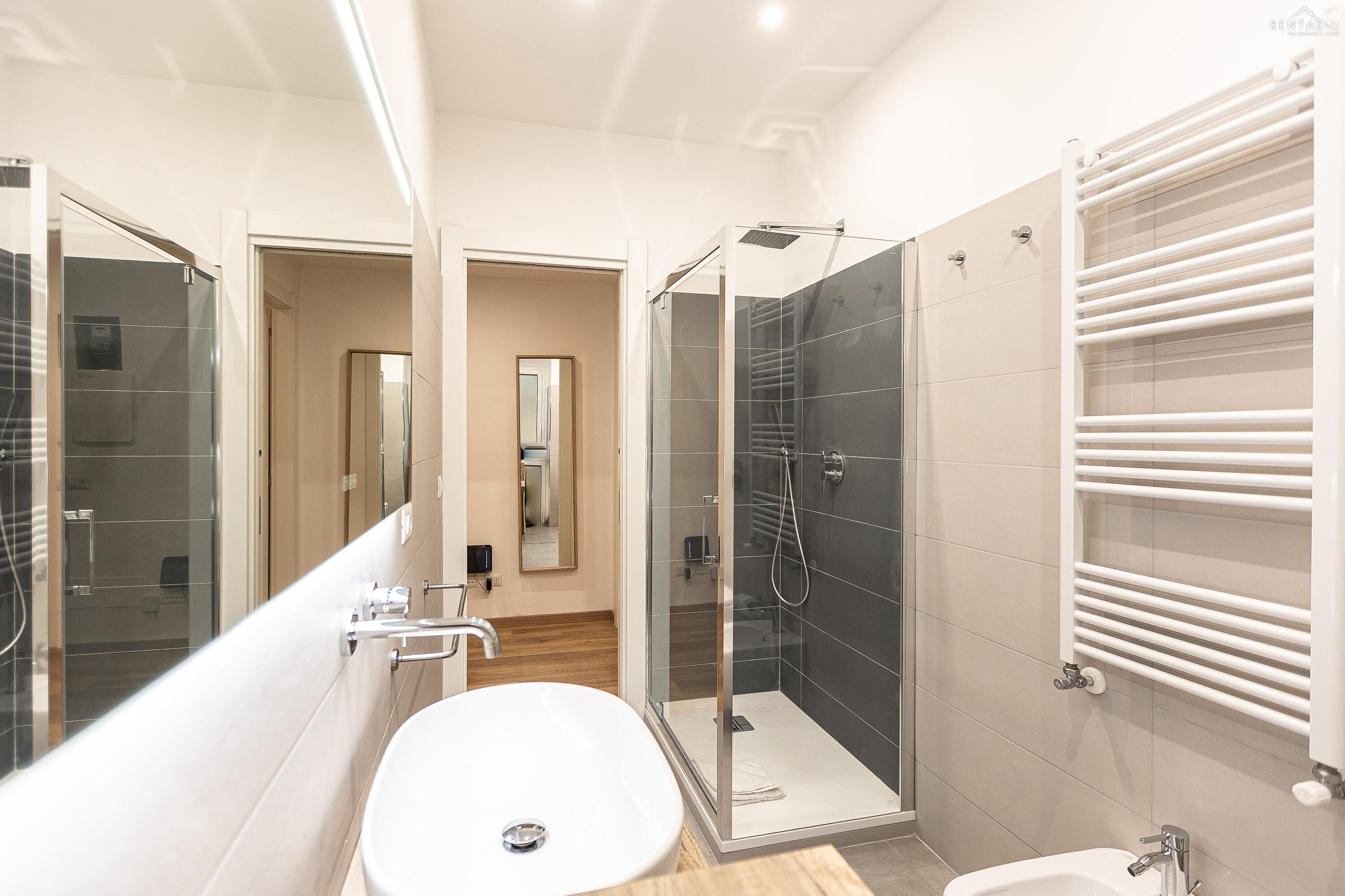 A modern bathroom with a large white sink, a glass-enclosed shower, and a white towel rack.