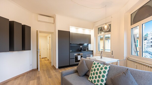 A modern apartment with a grey sofa, a kitchen area, and a dining table. - Rental in Rome Matilde Modern Apartment (Rome)