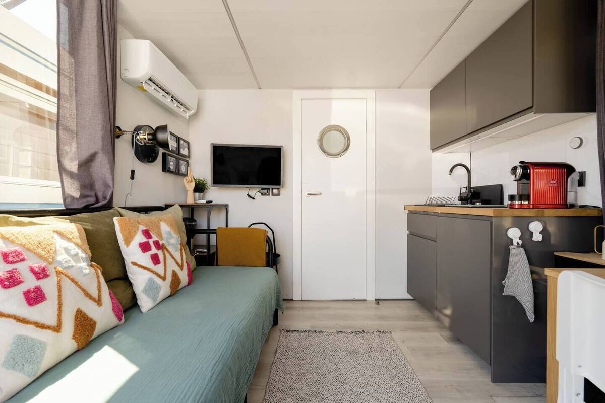 A compact living space with a bed, a small kitchenette, a television, and a window with curtains.