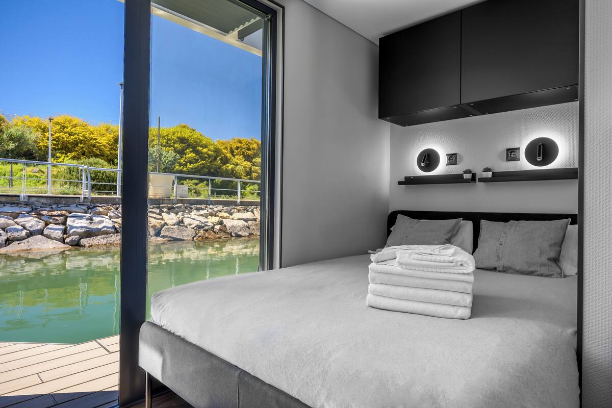A modern bedroom with a large bed, a view of a body of water, and built-in lighting.