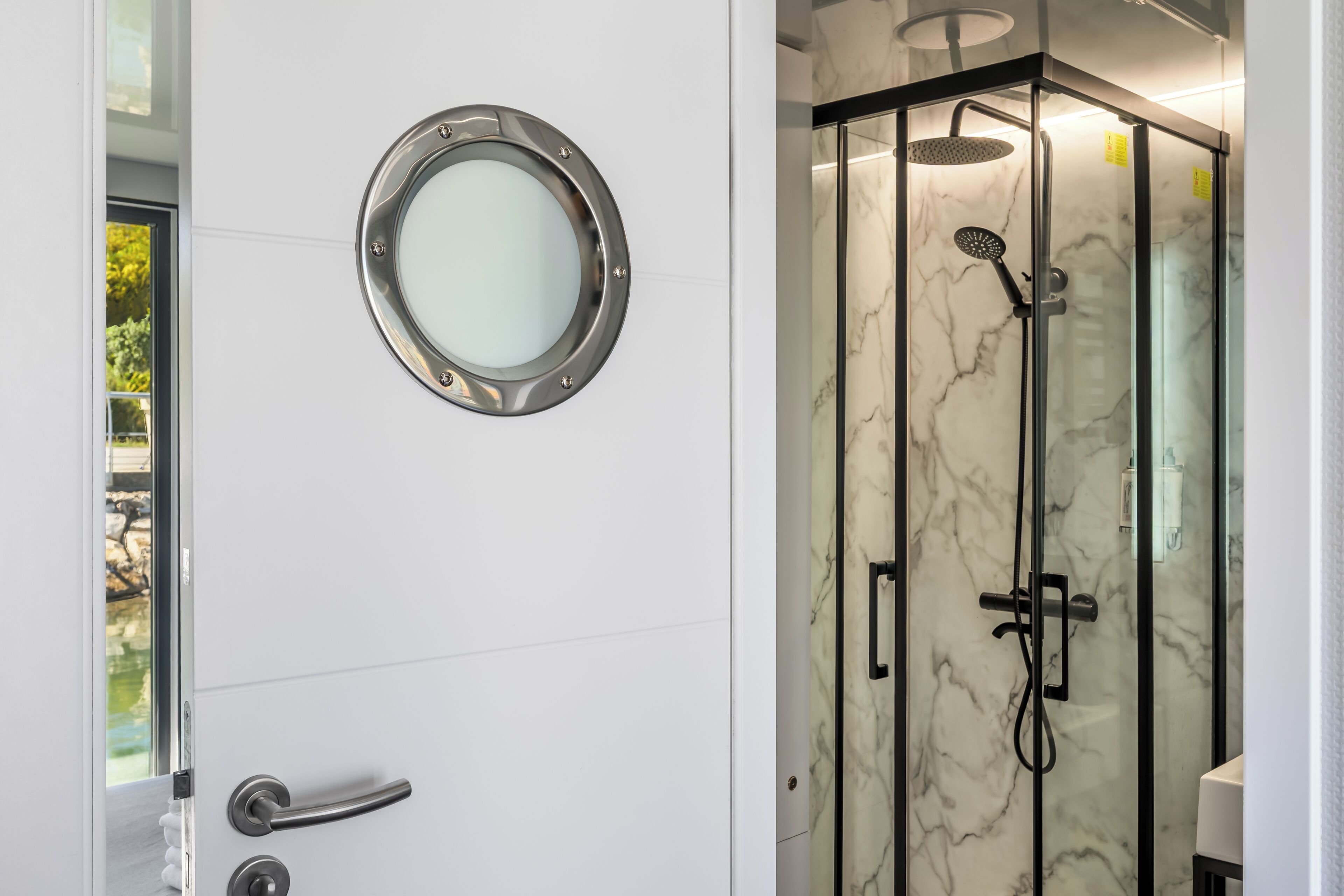Un baño con cabina de ducha de vidrio, un espejo redondo y una puerta con manija.