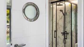 Un baño con cabina de ducha de vidrio, un espejo redondo y una puerta con manija.