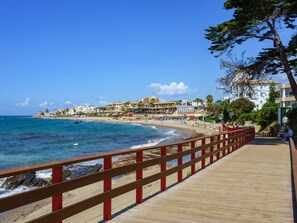 Une promenade en bois mène à une plage d’où l’on a une vue dégagée sur l’océan et sur les bâtiments qui se dressent à l’arrière-plan.