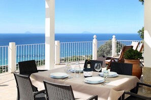 Mesa dispuesta para comer con vista al mar y un paisaje montañoso.