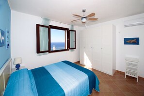 A bedroom with a bed, a ceiling fan, a wardrobe, and a window with a view. - Villa Dammuso is an exclusive villa where tranquility, privacy and comfort come together in a unique setting, surrounded by nature and overlooking the sea. The entire property is for your private use, including the beautiful infinity pool reserved solely (Caronia)