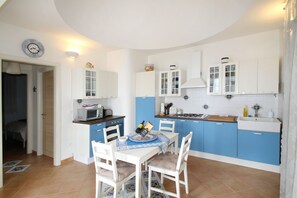A compact kitchen with white and blue cabinets, a dining table with chairs, and a microwave. - Villa Dammuso is an exclusive villa where tranquility, privacy and comfort come together in a unique setting, surrounded by nature and overlooking the sea. The entire property is for your private use, including the beautiful infinity pool reserved solely (Caronia)