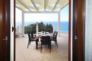 A covered outdoor dining area with a table set for four, overlooking the sea. - Villa Dammuso is an exclusive villa where tranquility, privacy and comfort come together in a unique setting, surrounded by nature and overlooking the sea. The entire property is for your private use, including the beautiful infinity pool reserved solely (Caronia)