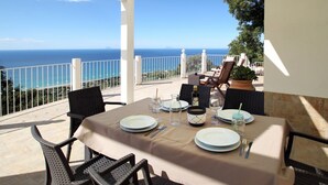 A terrace with a table set for dining, overlooking a coastal view. - Villa Dammuso is an exclusive villa where tranquility, privacy and comfort come together in a unique setting, surrounded by nature and overlooking the sea. The entire property is for your private use, including the beautiful infinity pool reserved solely (Caronia)