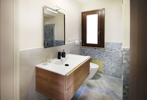 Un baño con tocador de madera, lavamanos blanco, espejo y un inodoro.