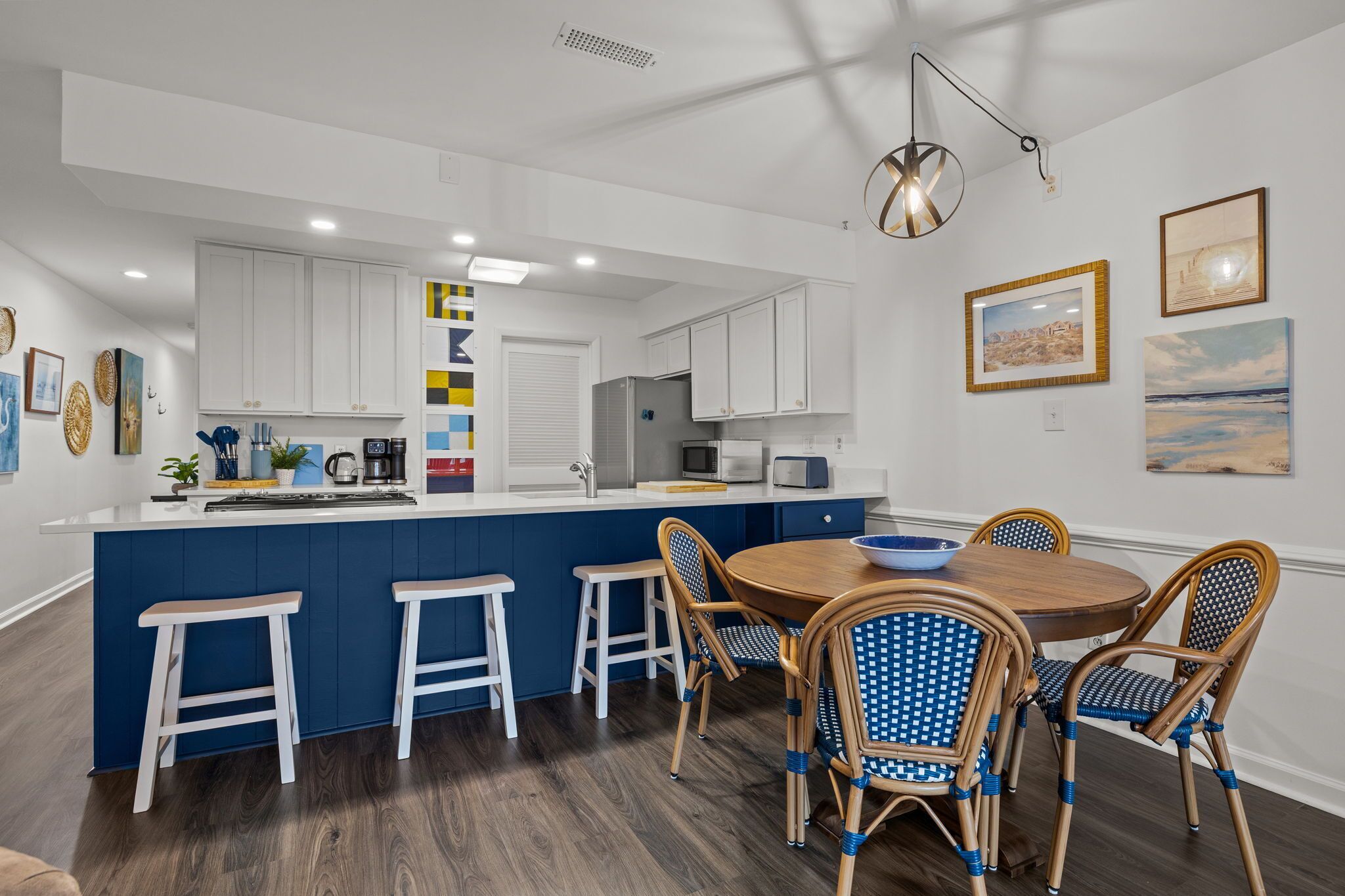 A modern kitchen with white cabinets, a blue island, and a dining area with wicker chairs and a wooden table.