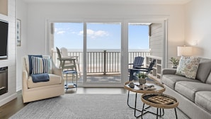 Ein geräumiges Wohnzimmer mit einer großen Schiebeglasdoor zum Balkon mit Meerblick. Es gibt ein beiges Sofa, ein graues Couche und zwei Korbtische.